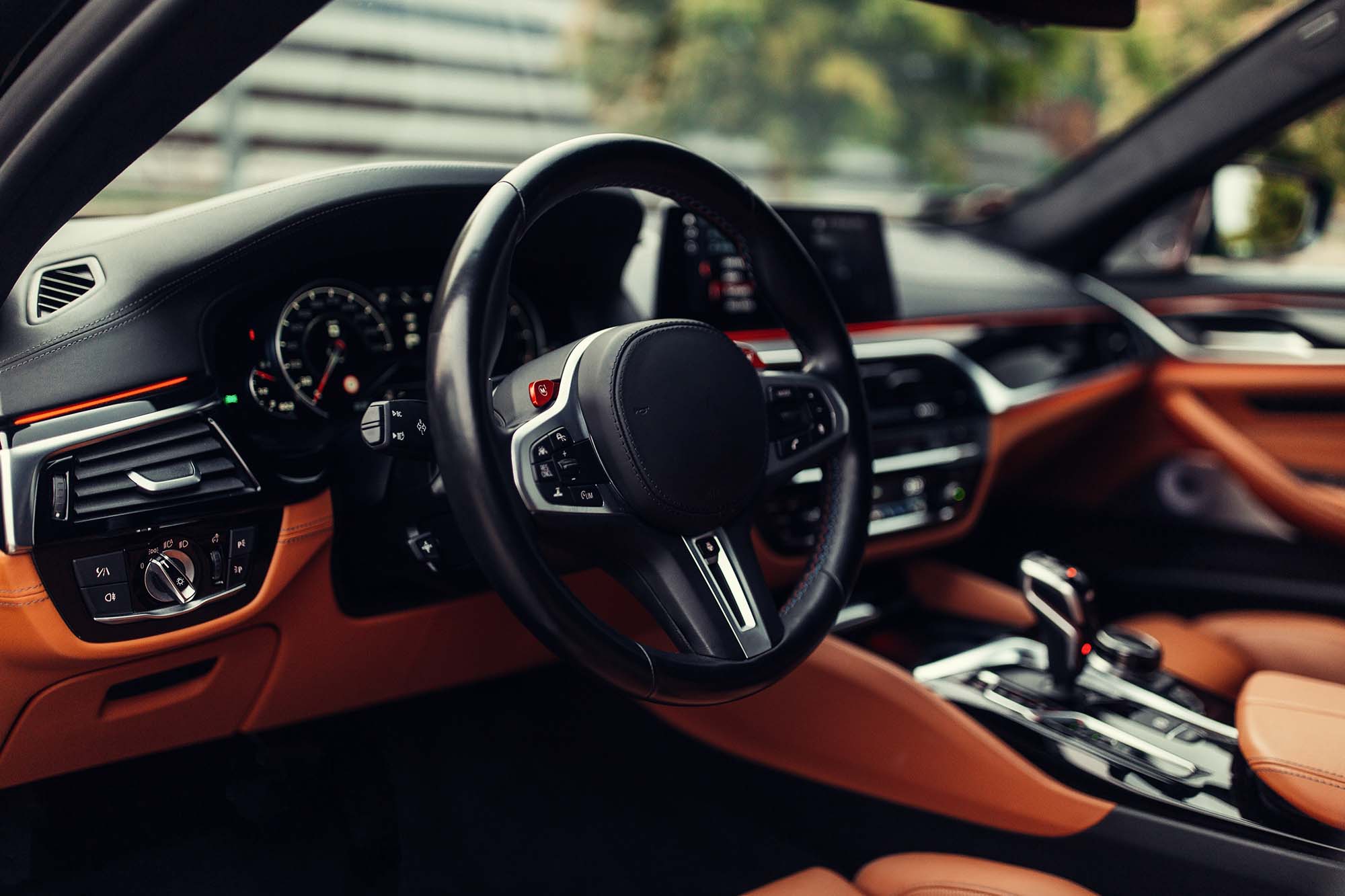 Interior of a luxury car featuring a black leather steering wheel, digital dashboard, and tan leather seats.