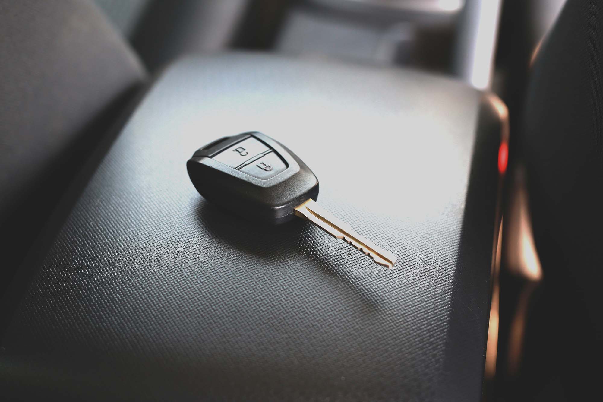 Car key with lock and unlock buttons resting on a textured black car seat.